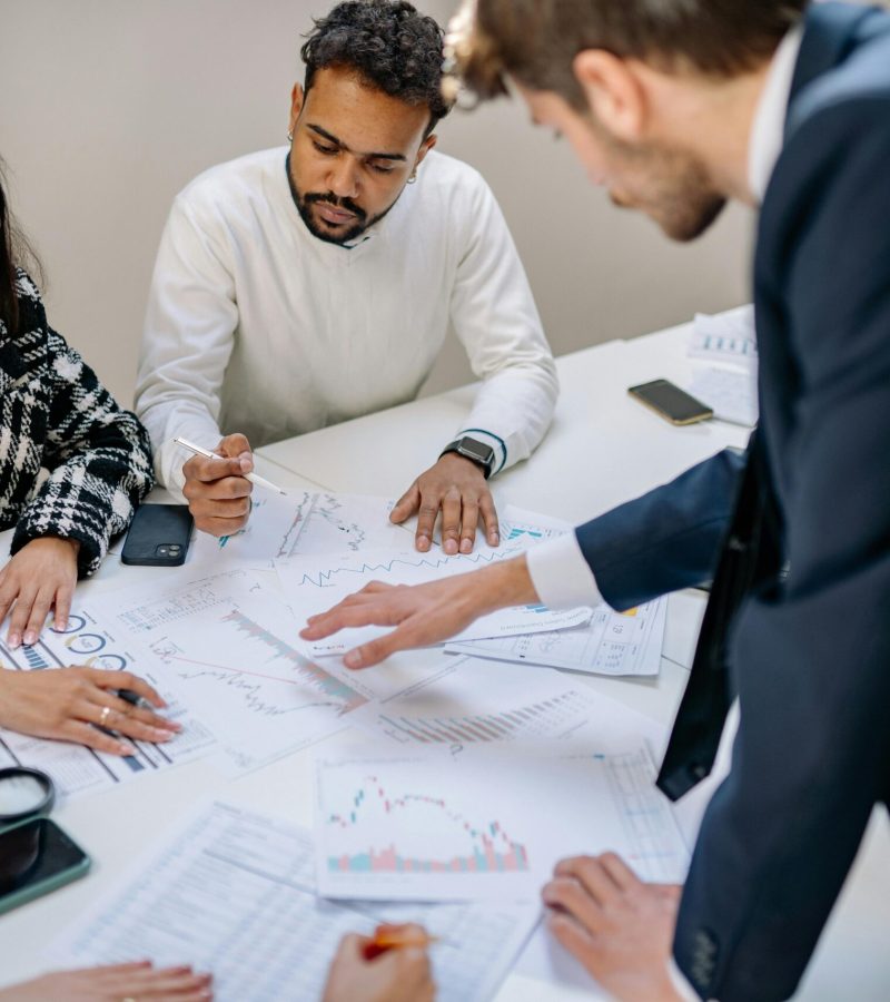 A diverse team collaborating in an office meeting, discussing papers with charts.